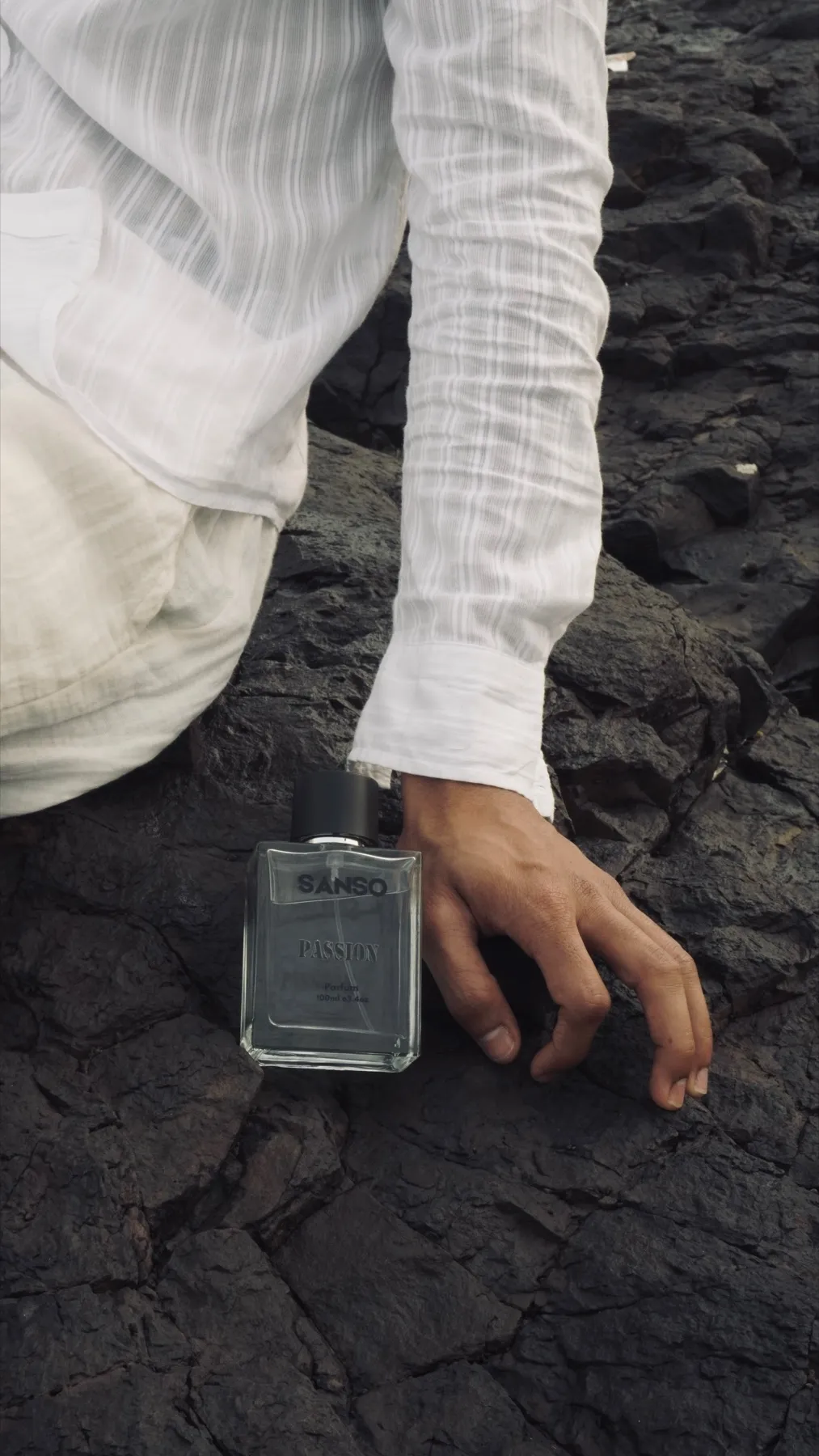Sanso Passion bottle standing on wet black rock beside a hand in a white linen sleeve