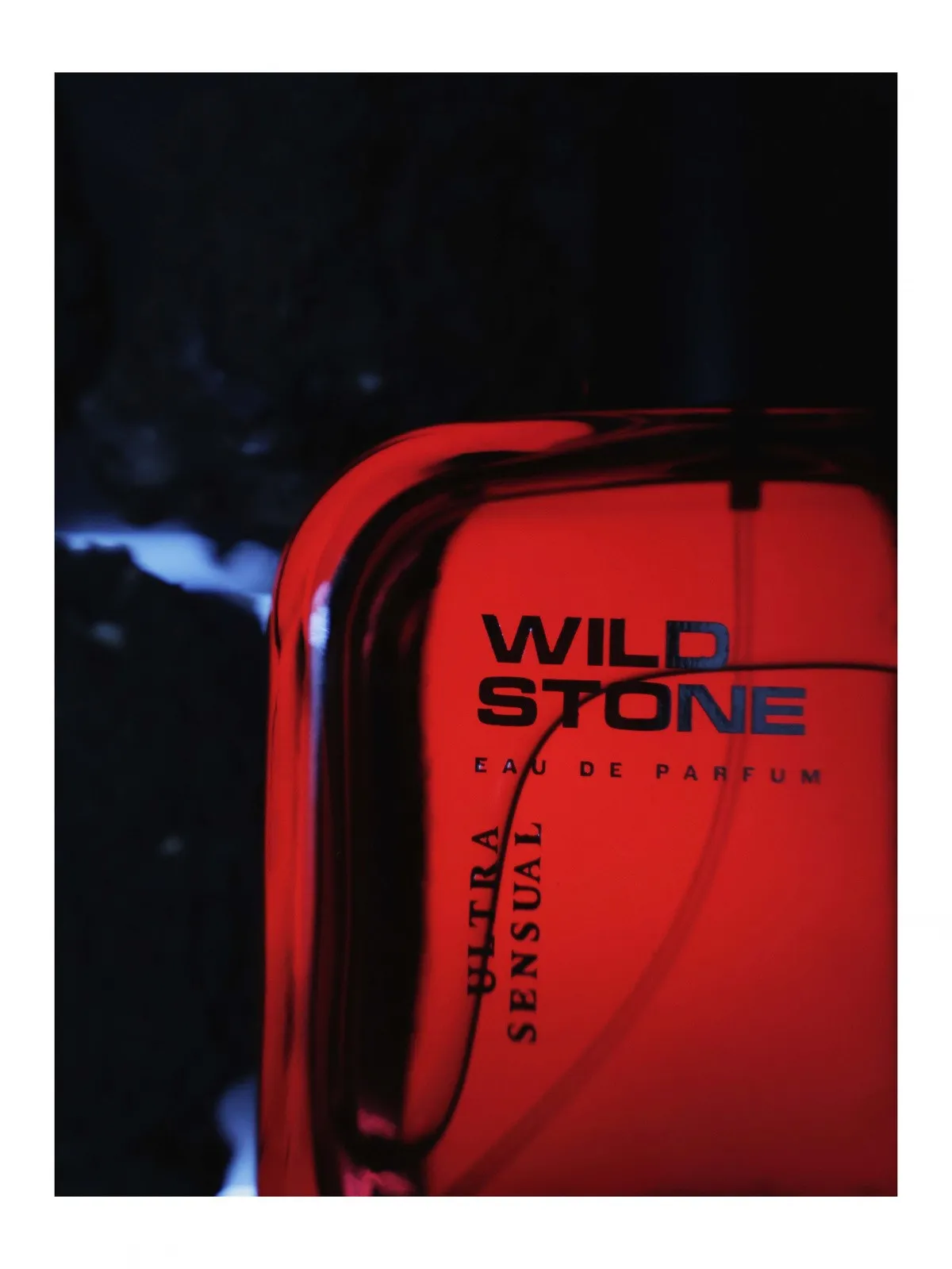 Close crop of the Wild Stone bottle edge with red light catching the glass